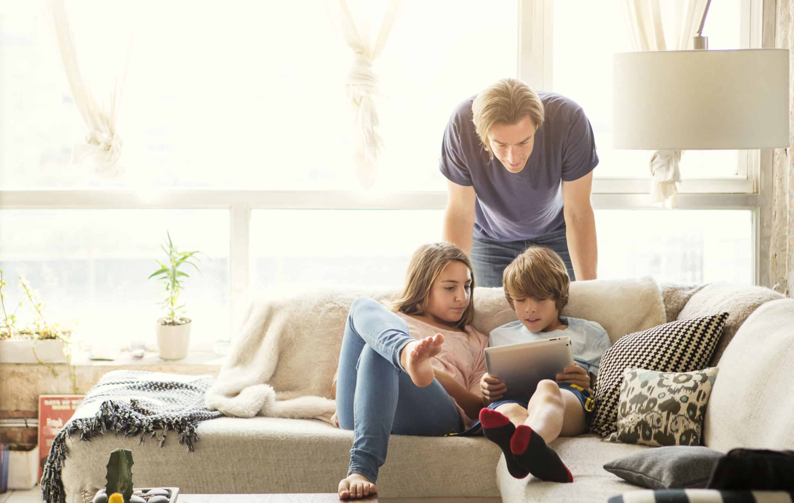 Father and two children sitting on a sofa using a tablet in a bright, cozy living room, powered by Castaways Energy solutions.