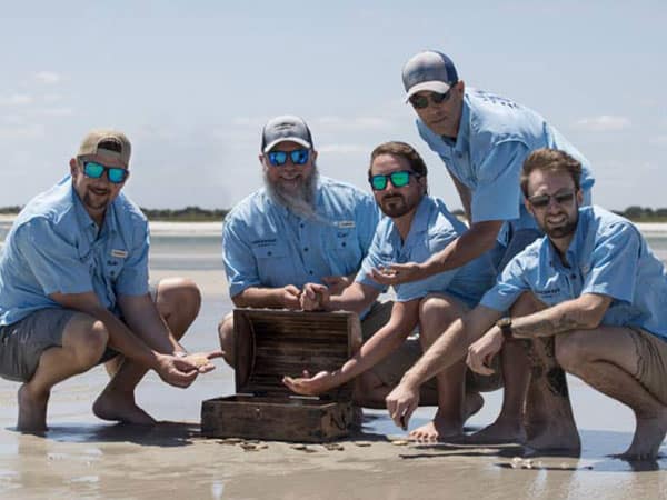 Castaways Energy team at the beach, posing with a treasure chest in the sand.