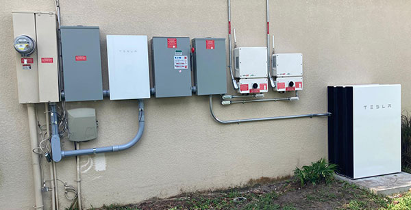 Tesla Powerwall and electrical panels installed on a home's exterior wall, provided by Castaways Energy, showcasing advanced home energy storage solutions.